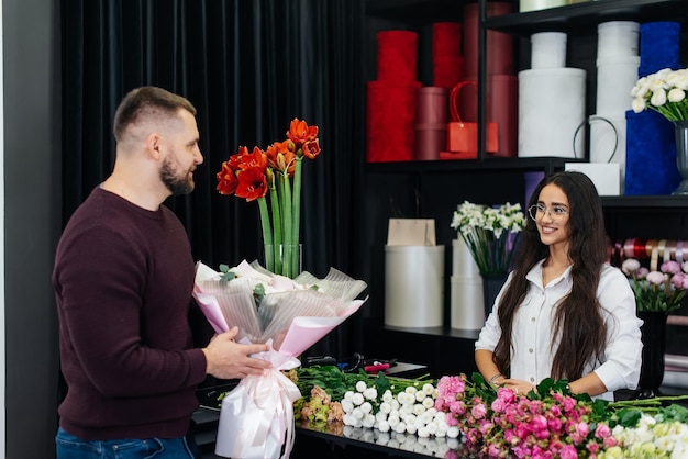 Um jovem barbudo compra um lindo buquê de flores para as férias de uma garota em uma aconchegante loja de flores Floricultura e buquê em uma floricultura Pequena empresa