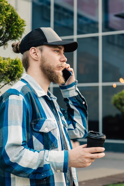 Um jovem barbudo está falando ao telefone e segurando uma xícara de café