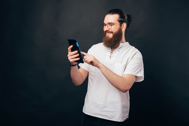 Um jovem barbudo está segurando um pc e sorrindo, digitando nele