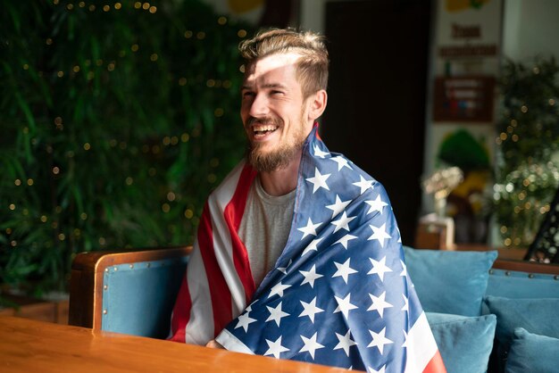 Um jovem barbudo feliz coberto com a bandeira americana dos eua