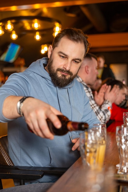 Um jovem bonito com barba derramando cerveja de garrafa em copos