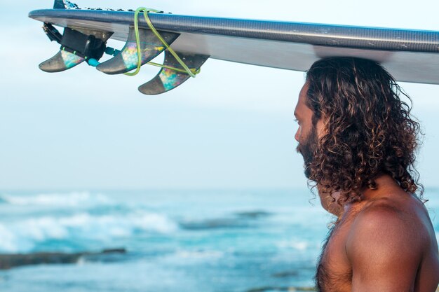 Um jovem bonito de pele escura com uma prancha de surf