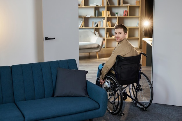 Foto um jovem bonito em uma cadeira de rodas se move pelo apartamento se acostumando com uma nova vida recuperação após lesão ou doença solitária em casa