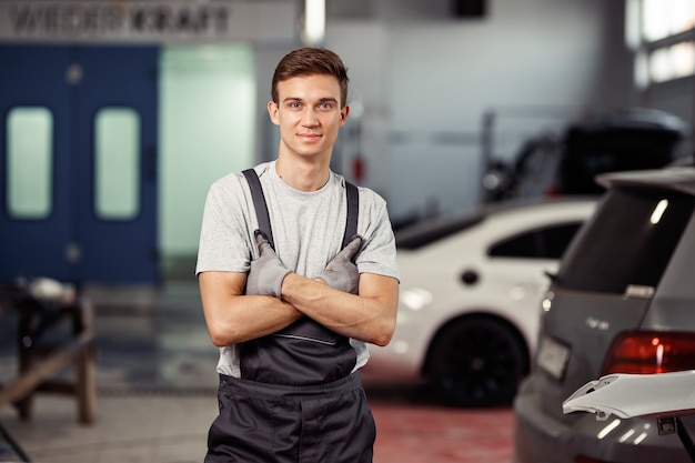 Um jovem bonito está perto de carros em uma oficina de automóveis.