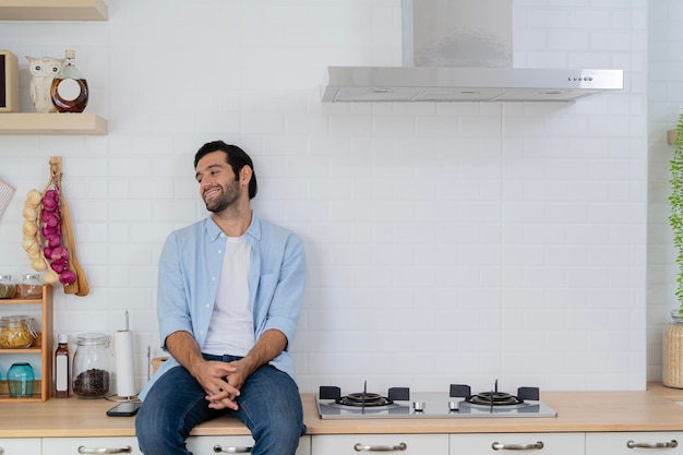 Um jovem bonito olha pela janela enquanto se senta no balcão da cozinha