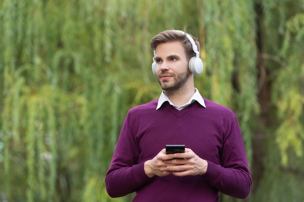 Um jovem bonito ouve música em fones de ouvido e conversa no telefone ao ar livre