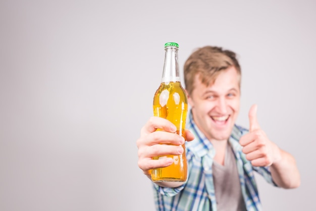 Foto um jovem bonito se sentindo feliz mostrando os polegares e segurando uma garrafa de cerveja.