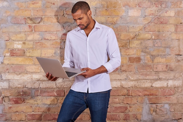 Um jovem bonito sério usando um laptop em uma camisa branca.