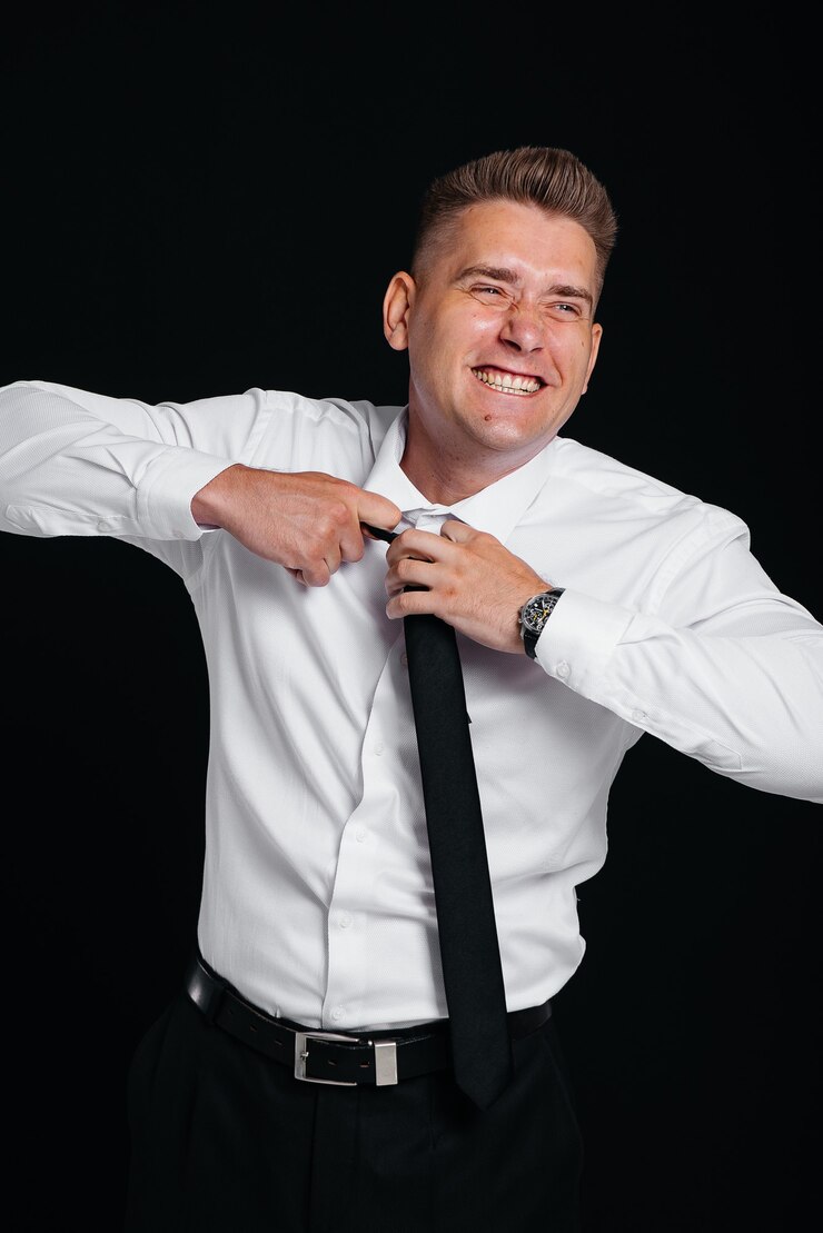 Foto um jovem bonito tira a gravata e ri, posando em um fundo preto. um homem de negócios elegante. um grande empresário.