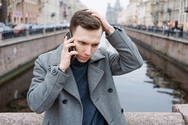 Um jovem bonito usando telefone celular vestindo um elegante casaco cinza fica