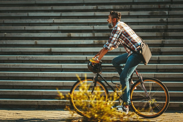 Um jovem bonito vai para a cidade com sua bicicleta. Ele está andando de moto, feliz por causa do bom tempo.