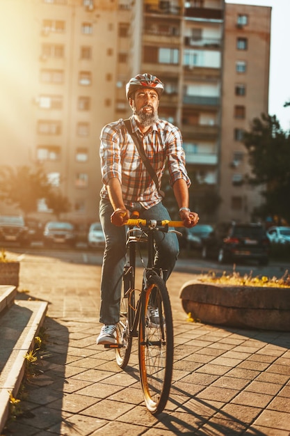 Um jovem bonito vai para a cidade com sua bicicleta. ele está andando de moto, feliz por causa do bom tempo.