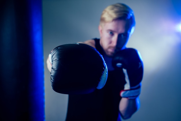 Um jovem boxeador masculino está praticando esportes no ginásio. boxeador, luvas de boxe em um fundo escuro. homem ataca