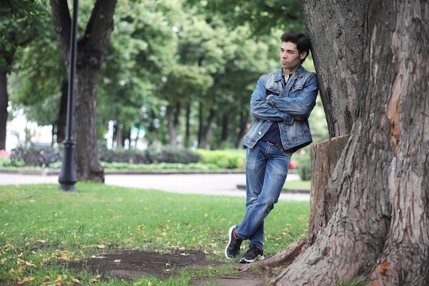 Um jovem caminha no parque na hora do almoço. Um homem está passeando pela cidade. Um estudante no parque.