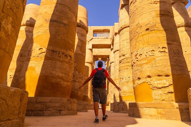 Um jovem caminhando entre as colunas com hieróglifos dentro do templo de karnak