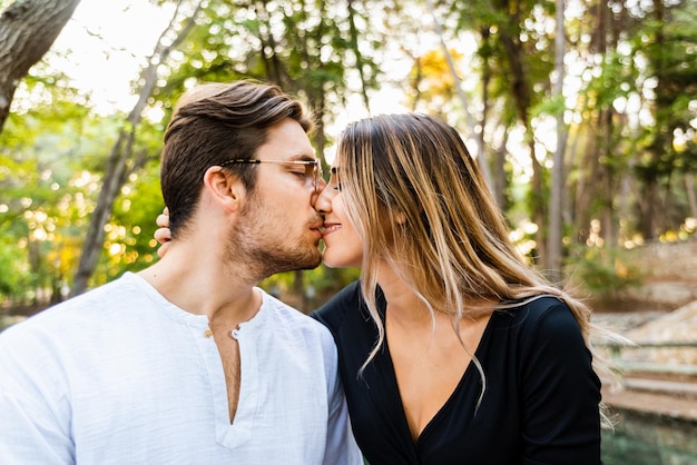 Um jovem casal a beijar-se contra as árvores.