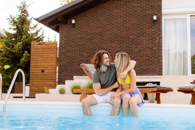 Um jovem casal a relaxar à beira da piscina no quintal da casa.