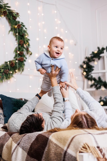 Um jovem casal alegre com um filho pequeno está brincando na cama perto da árvore de Natal Interior de Ano Novo no quarto Árvore de Natal com brinquedos Atmosfera familiar festiva