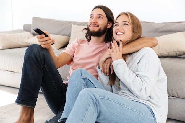 Um jovem casal amoroso feliz no sofá assistir a um filme de tv dentro de casa, em casa.