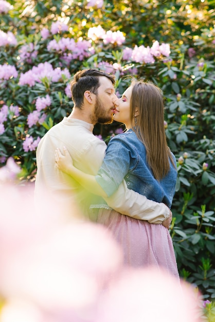 Um jovem casal apaixonado cara e menina beijam no fundo de um rododendro em flor. Primeiro encontro. Dia dos namorados