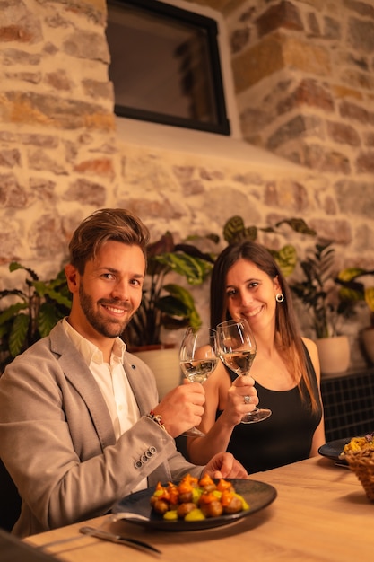 Um jovem casal apaixonado em um restaurante, brindando taças de vinho, comemorando o Dia dos Namorados, foto vertical