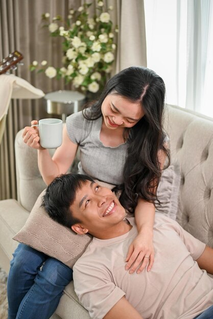 Um jovem casal asiático feliz gosta de conversar e relaxar juntos num sofá na sala de estar