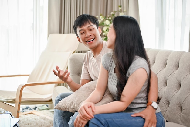 Um jovem casal asiático feliz gosta de conversar num sofá na sala de estar.