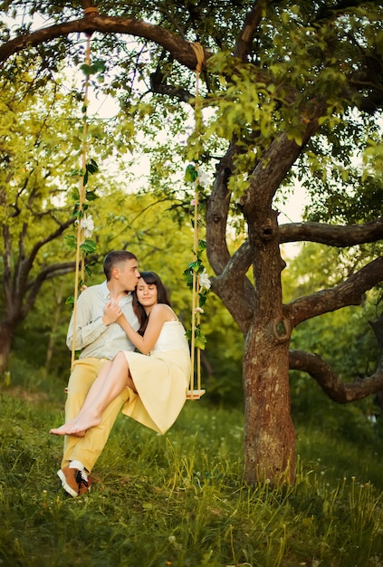 Um jovem casal beija no parque no balanço da árvore