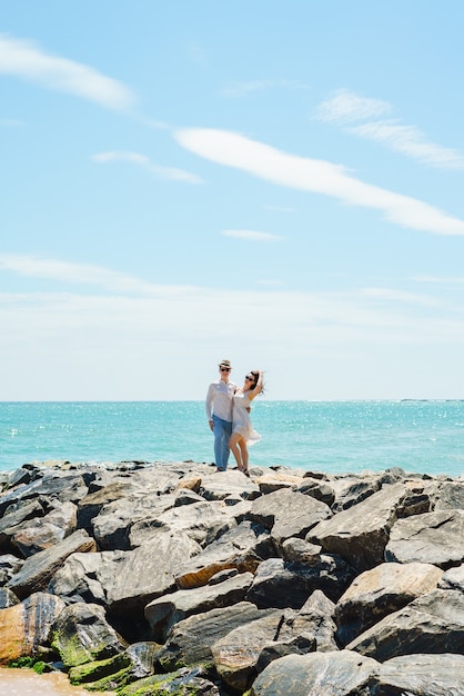 Um jovem casal de namorados, um cara e uma garota no oceano com roupas brancas nas pedras