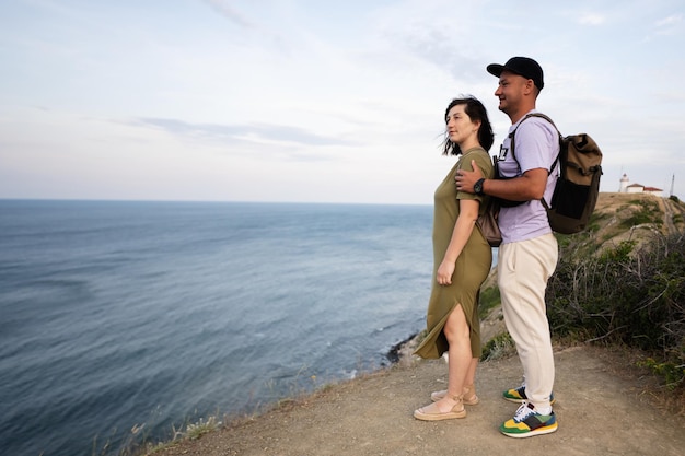 Um jovem casal de pé na borda de um penhasco e olhando para o mar