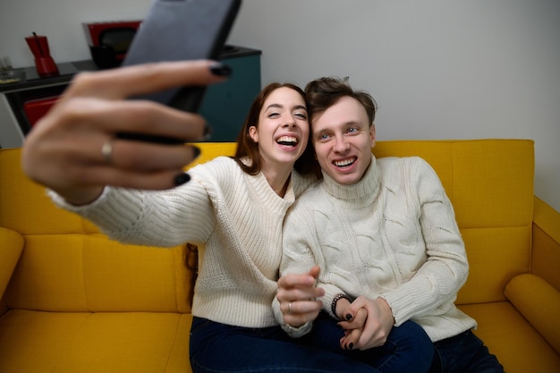 Um jovem casal em casa, eles se sentam no sofá e tiram selfies