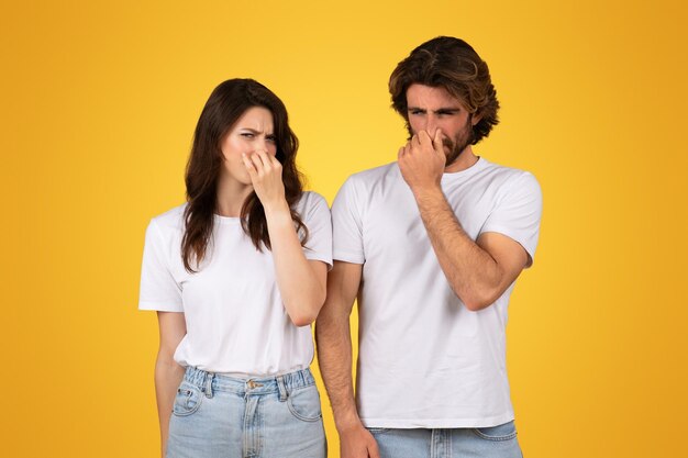 Um jovem casal em dificuldades com camisas brancas apertando o nariz mostrando expressões de desgosto