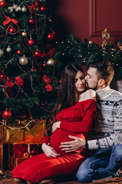 Um jovem casal espera por um milagre Um homem e uma esposa grávida no fundo de uma árvore de Natal