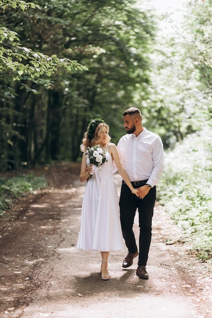 Um jovem casal feliz apaixonado anda em um jardim Um homem de camisa branca e uma garota de vestido branco claro estão andando em um parque