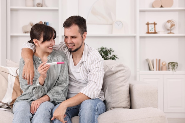 Um jovem casal feliz com um teste de gravidez no sofá em casa, espaço para mensagens de texto.