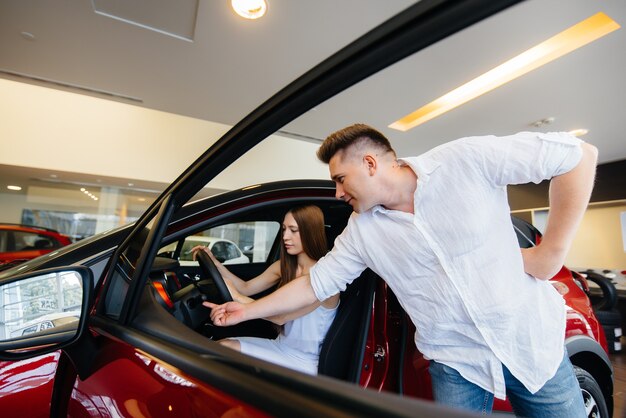 Um jovem casal feliz escolhe e compra um carro novo em uma concessionária. comprando um carro novo.