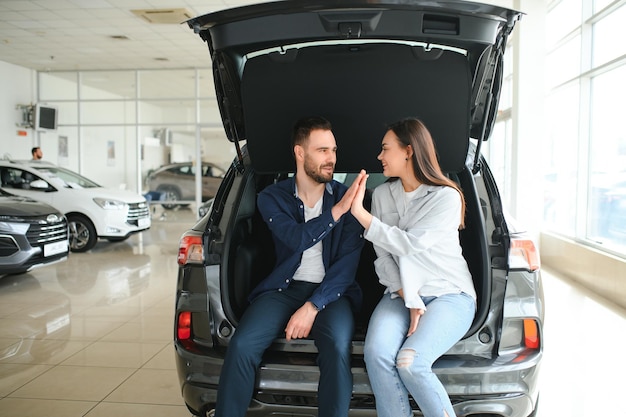 Um jovem casal feliz escolhe e compra um carro novo para a família visitando a concessionária