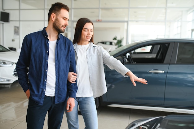 Um jovem casal feliz escolhe e compra um carro novo para a família visitando a concessionária