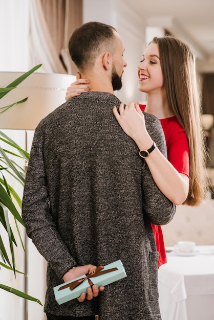 Um jovem casal feliz no restaurante e um jovem escondem uma pequena caixa com presente