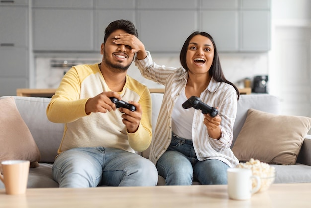 Um jovem casal indiano alegre se divertindo em casa jogando videogames juntos