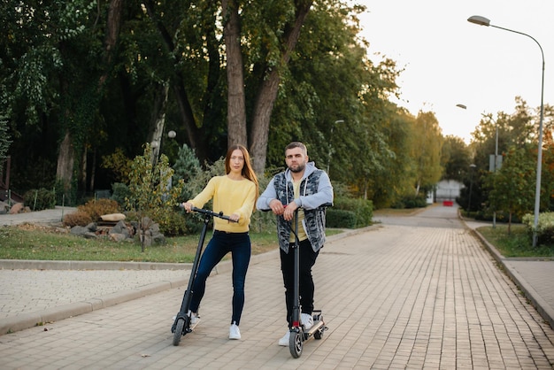 Um jovem casal lindo anda de scooters elétricas no parque em um dia quente de outono. hobbies e recreação.