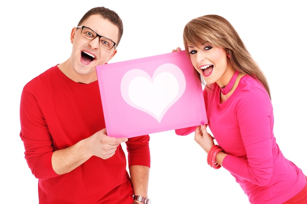 um jovem casal mostrando uma placa rosa com um coração sobre fundo branco