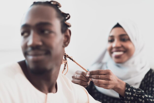 Um jovem casal muçulmano tem um momento romântico em casa enquanto a mulher faz o penteado para o marido feminino vestindo roupas tradicionais do hijab islâmico do Sudão. Foto de alta qualidade