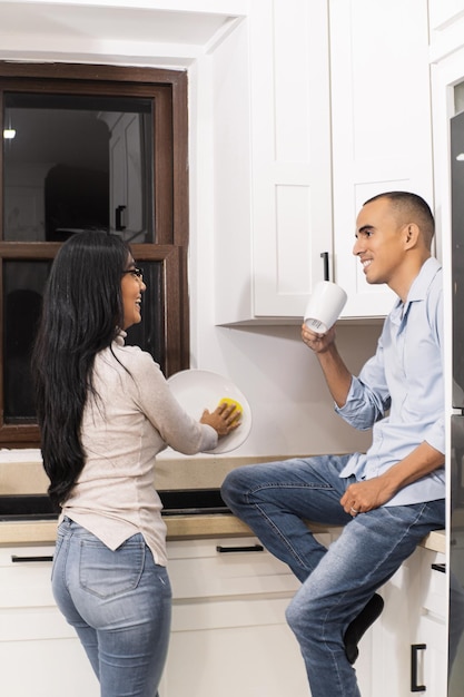 Um jovem casal na cozinha conversando e limpando a louça