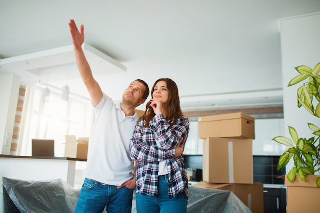 Um jovem casal na sala de estar fica perto de caixas desempacotadas.