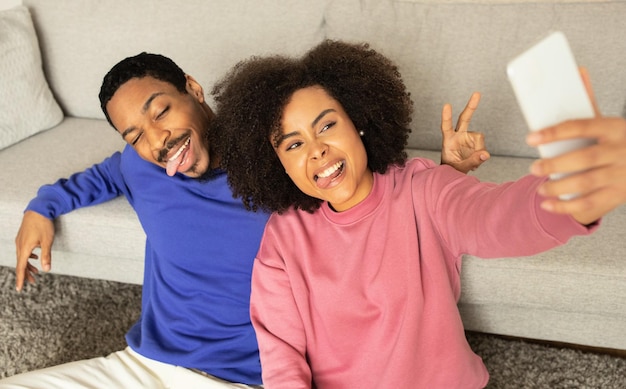 Um jovem casal negro capturando o momento com uma selfie em um smartphone dentro de casa