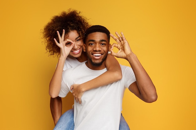 Um jovem casal preto a andar de costas mostrando um gesto de "ok"