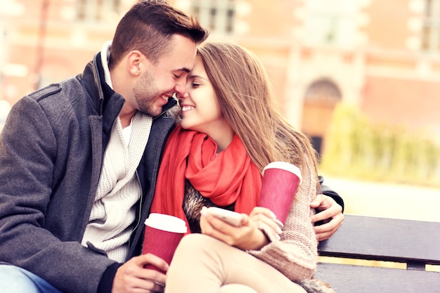 um jovem casal romântico se beijando em um banco com smartphone no parque