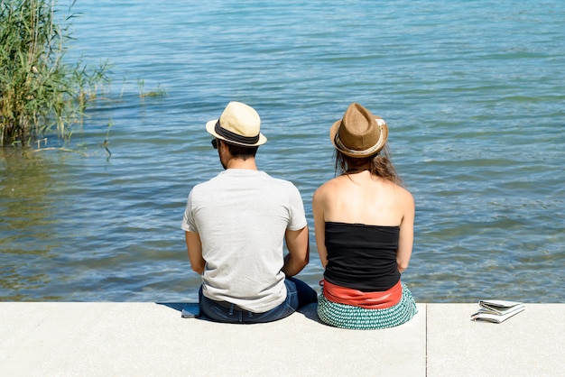 Um jovem casal sentado à beira-mar, vista traseira