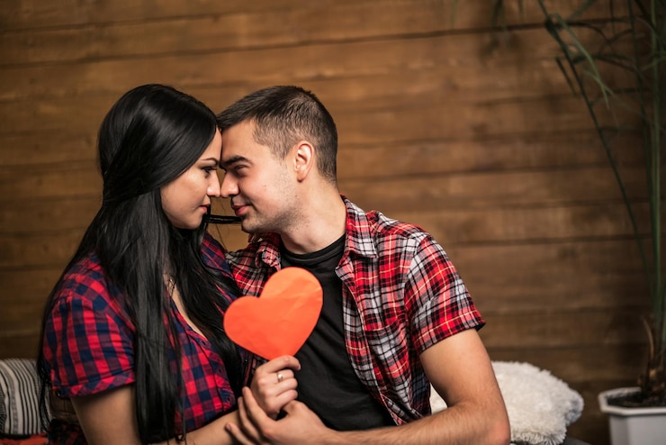 Foto um jovem casal sentado no chão com um coração vermelho nas mãos.